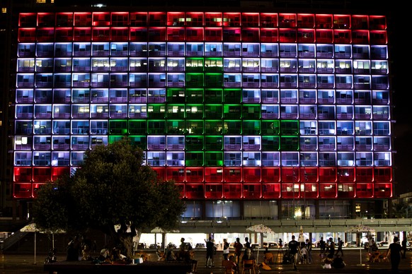 People hang out at Rabin square as the municipality building is lit in the colours of the Lebanese flag, in a rare show of Israeli solidarity with Beirut as it reels from a devastating explosion, in T ...