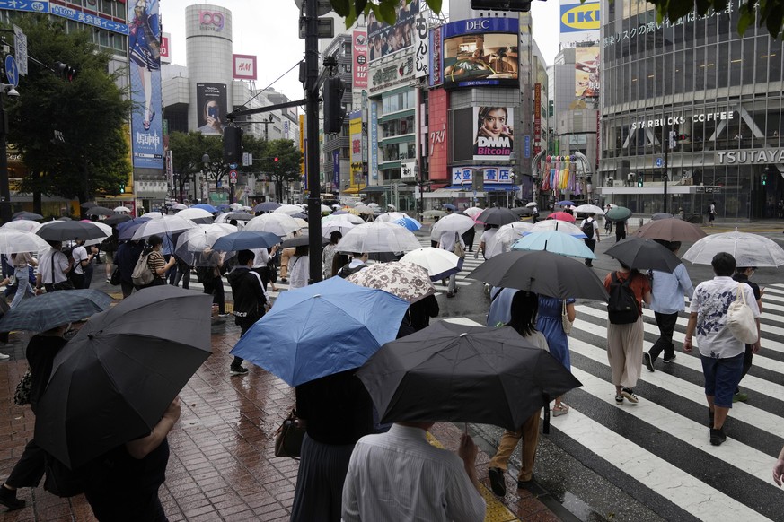 Morning commuters with umbrella cover a crosswalk Tuesday, July 27, 2021, in Tokyo. The rains have come to Tokyo and its Olympics. After many days of blistering sunshine, the rain cooled Tokyo by abou ...