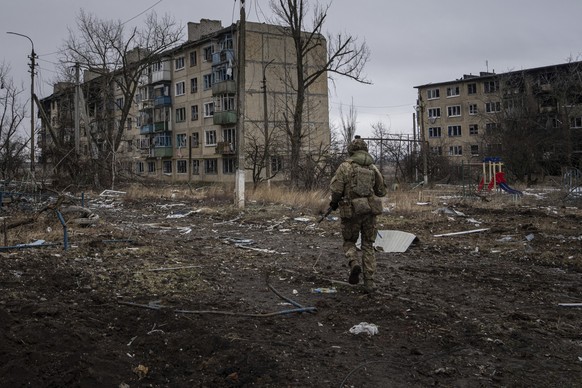 25.02.2023, Ukraine, Wuhledar: Ein ukrainischer Marinesoldat geht an zerstörten Wohnblocks vorbei. Foto: Evgeniy Maloletka/AP/dpa +++ dpa-Bildfunk +++