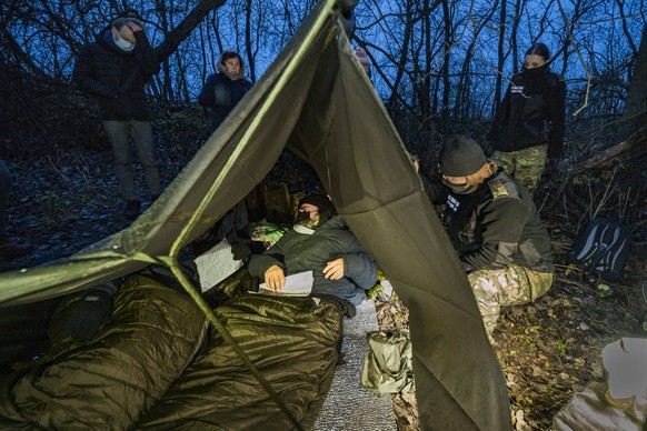 Syrian migrants in the forests of Poland after crossing illegally the border from Belarus. A polish border guard checks two syrian refugees under a plastic cover in the forests of Poland. They ask for ...
