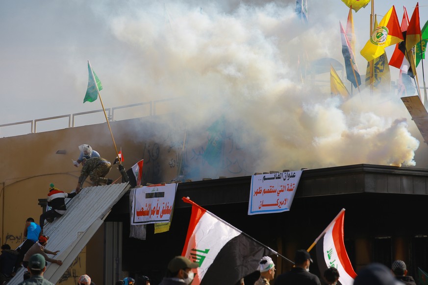 Anhänger und Demonstranten der schiitischen Miliz im Irak stehen mit Fahnen vor Botschaft der Vereinigten Staaten, nachdem sie ein Feuer gelegt haben. 