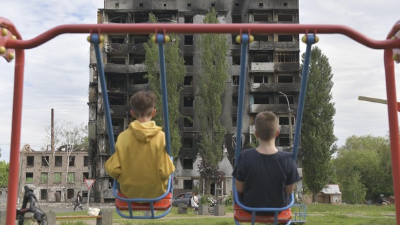 02.06.2022, Ukraine, Kiew: Zwei Kinder sitzen auf einer Schaukel und blicken auf ein durch russische Militärangriffe ausgebranntes mehrstöckiges Wohngebäude. Foto: -/kyodo/dpa +++ dpa-Bildfunk +++