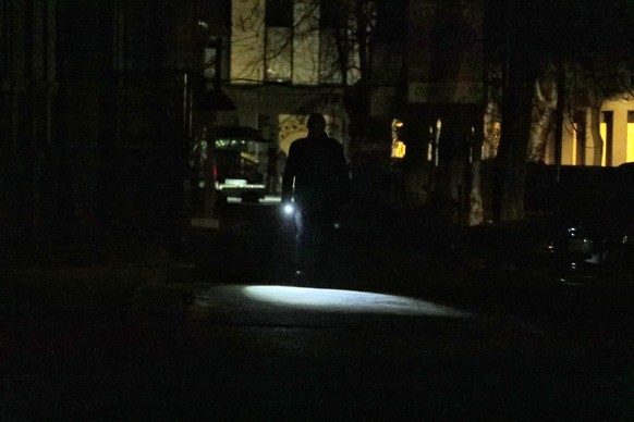 05.12.2022, Ukraine, Odessa: Ein Mann leuchtet sich den Weg mit einer Taschenlampe in einer dunklen Stra