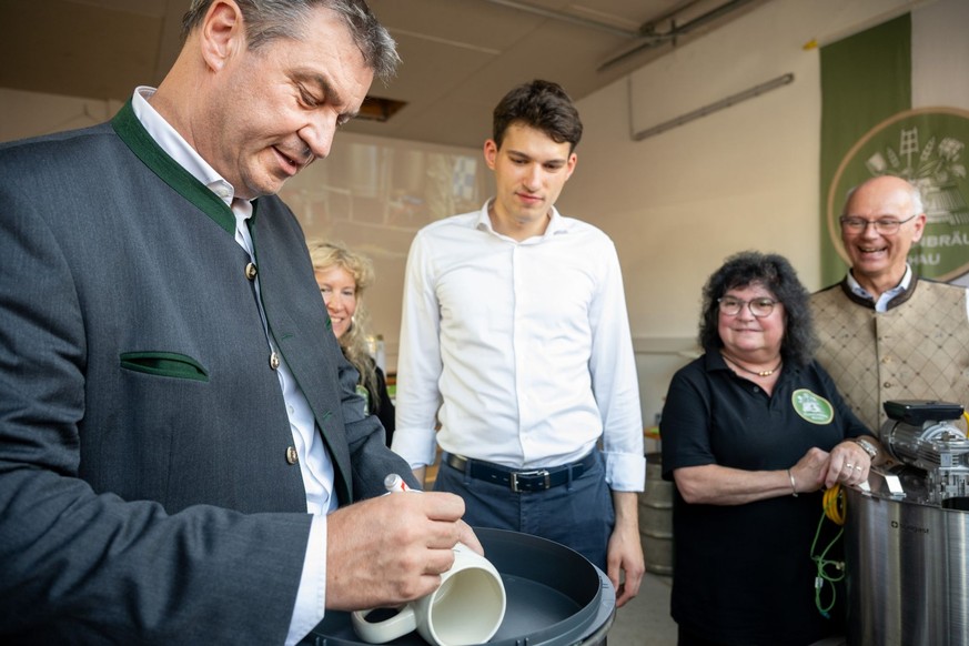 20.08.2023, Bayern, Hallerstein: Der Bayerische Ministerpräsident Markus Söder (CSU) siginiert einen Krug der Kommunbräu Rehau beim 19. Hallersteiner Handwerkermarkt. Foto: Pia Bayer/dpa +++ dpa-Bildf ...