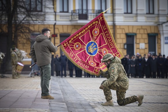 HANDOUT - 24.02.2023, Ukraine, Kiew: Wolodymyr Selenskyj (l), Präsident der Ukraine, hält eine Fahne einer Militäreinheit, die von einem Offizier geküsst wird, während einer Gedenkveranstaltung. Die r ...