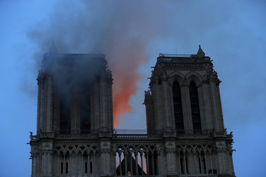 Smoke and flames fill the sky as a fire burns at the Notre Dame Cathedral during the visit by French President Emmanuel Macron in Paris, Monday, April 15, 2019. A catastrophic fire engulfed the upper  ...