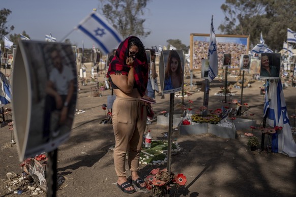 20.06.2024, Israel, Kibbuz Re&#039;im: Eine Frau steht neben Fotos von Menschen, die von militanten Hamas-Kämpfern während ihres gewaltsamen Amoklaufs beim Nova-Musikfestival im Süden Israels getötet  ...