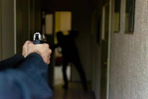 Action portrait of serious young detective, special agent, holding gun pointing the weapon, involved in shooting, entering in the the hallway in some bulding with caution, looking for and arresting a  ...