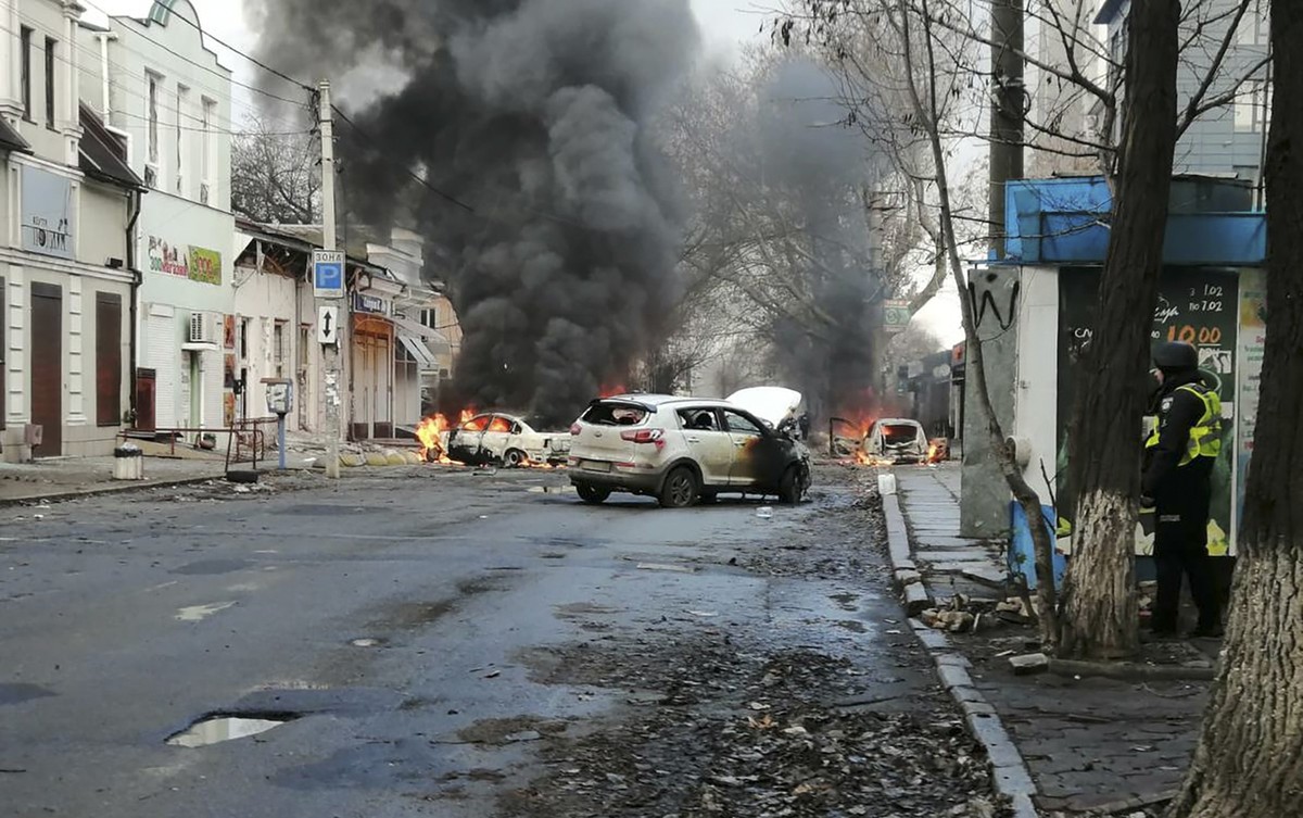 24.12.2022, Ukraine, Cherson: Autos brennen und Rauch steigt auf, nachdem ein russischer Raketenangriff das Stadtzentrum getroffen hat. Bei einem russischem Beschuss des Zentrums der südukrainischen S ...