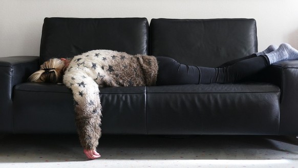 A senior woman lies on her stomach on the sofa with the left arm hanging down to the floor