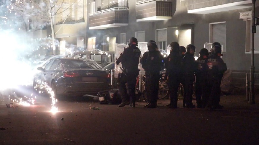 31.12.2022, Berlin: Polizeibeamte stehen hinter explodierendem Feuerwerk. Nach Angriffen auf Einsatzkräfte in der Silvesternacht hat die Diskussion um Konsequenzen begonnen. Berlins Regierende Bürgerm ...