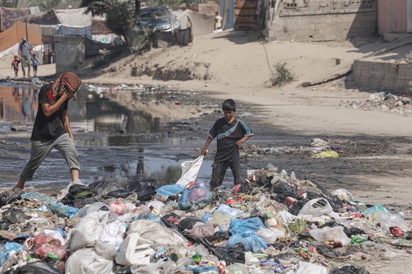 dpatopbilder - 22.07.2024, Pal�stinensische Gebiete, Deir el-Balah: Pal�stinenser gehen �ber M�ll in der N�he von Zelten, die als Unterschlupf in einer mit stehendem Abwasser bedeckten Stra�e dienen.  ...