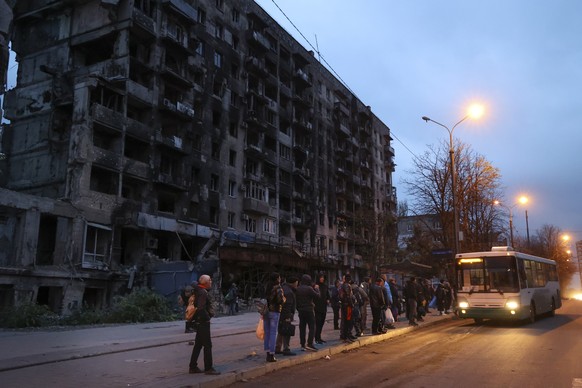 04.11.2022, Ukraine, Mariupol: Menschen warten an einer Bushaltestelle vor einem bei schweren Kämpfen beschädigten Wohnhaus. Foto: Alexei Alexandrov/ap/dpa +++ dpa-Bildfunk +++