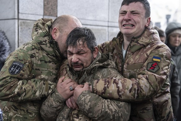 15.12.2023, Ukraine, Kiew: Ukrainische Soldaten weinen neben dem Sarg ihres Kameraden Andrii Trachuk während seiner Trauerfeier auf dem Unabhängigkeitsplatz. Trachuk war ein Veteran der Revolution der ...