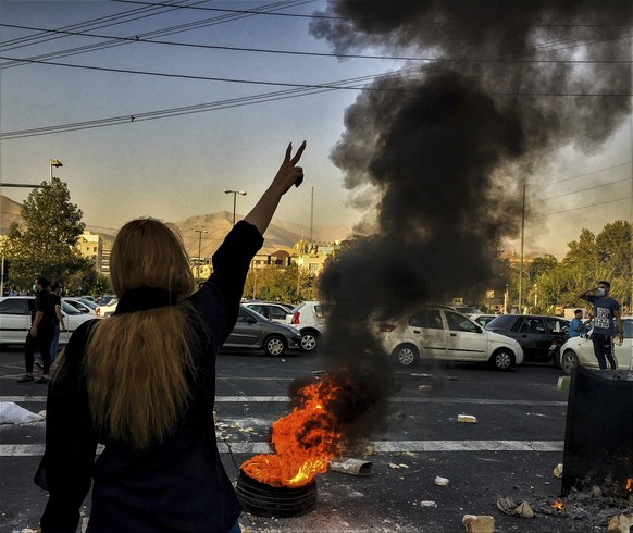 ARCHIV - 30.09.2022, Iran, Teheran: Eine Frau steht w�hrend einer Demonstration nach dem Tod der 22-j�hrigen Mahsa Amini vor einem brennenden Autoreifen und zeigt das Victory-Zeichen. Die 22-j�hrige F ...