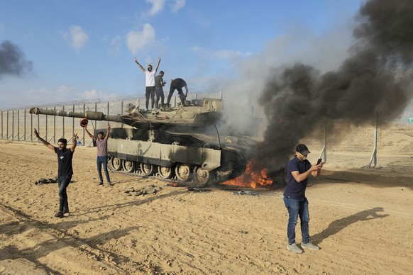 07.10.2023, Palästinensische Gebiete, Khan Younis: Palästinenser feiern an einem zerstörten israelischen Panzer am Zaun des Gazastreifens östlich von Khan Younis. Die islamistische Hamas hat vom Gazas ...