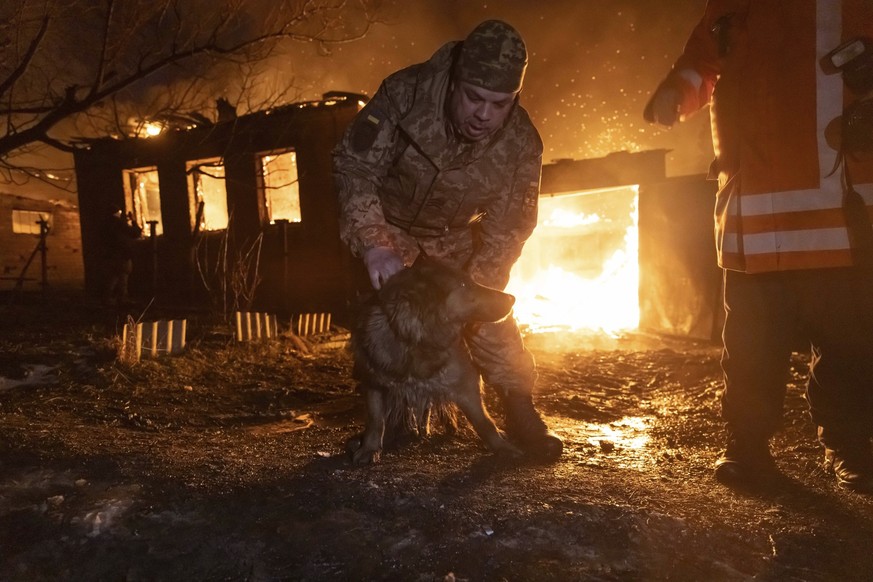 dpatopbilder - 10.02.2024, Ukraine, Charkiw: Ein Feuerwehrmann retten einen Hund, während sie ein Feuer nach einem russischen Angriff auf ein Wohnviertel löschen. Foto: Yevhen Titov/AP/dpa +++ dpa-Bil ...