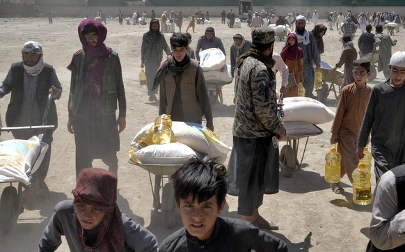 FILE - A Taliban fighter stands guard as people receive food rations distributed by a Chinese humanitarian aid group, in Kabul, Afghanistan, Saturday, April 30, 2022. Afghanistan is expected 1.1 milli ...