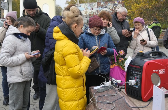 People charge their phones, try to connect to the internet and make phone calls on central square in Kherson, Ukraine, Thursday, Nov. 17, 2022. Russian airstrikes targeted Ukraine's energy facilities ...