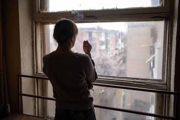 April 18, 2022, Kharkiv, Kharkiv Oblast, Ukraine: A woman smokes a cigarette while looking out of the window of a building damaged by Russian shelling in Kharkiv. Russia invaded Ukraine on 24 February ...