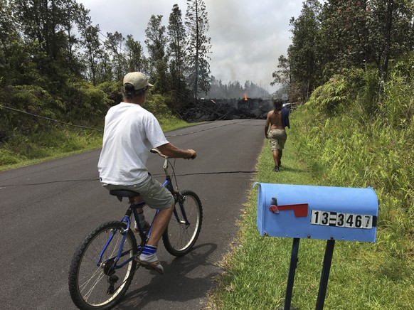 Resident Sam Knox rides his bicycle to the edge of the road as lava burns across the road in the Leilani Estates in Pahoa, Hawaii, Saturday, May 5, 2018. Hundreds of anxious residents on the Big Islan ...
