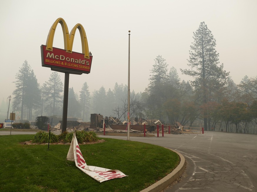 13.11.2018, USA, Paradise: Ein Hinweisschild auf die Filiale einer Fastfoodkette und ausgebrannte Trümmer nach dem Waldbrand, dem sogenannten «Camp»-Feuer. (zu dpa &quot;Paradise als Hölle auf Erden - ...