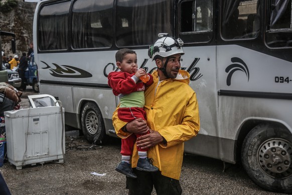 Ein Mitglied des syrischen Zivilschutzes "Weißhelme" trägt in Damaskus ein Kind auf dem Arm