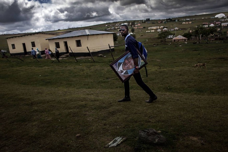 A man walks through the village of Qunu with a poster of Mandela as the funeral for former South African President Nelson Mandela can be seen in the background. PUBLICATIONxINxGERxSUIxAUTxONLY - ZUMAl ...