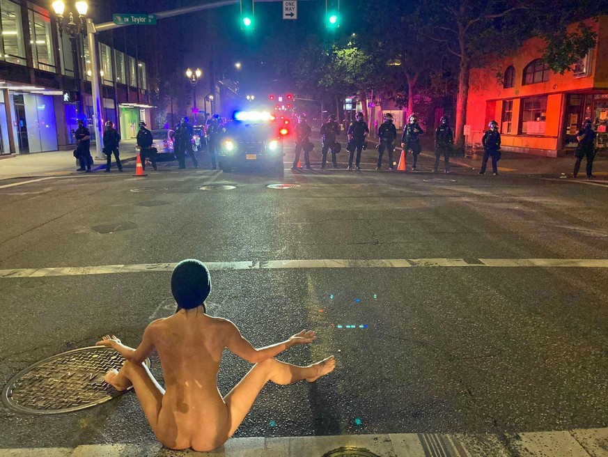 Eine entblößte Demonstrantin sitzt in Portland vor Polizisten.