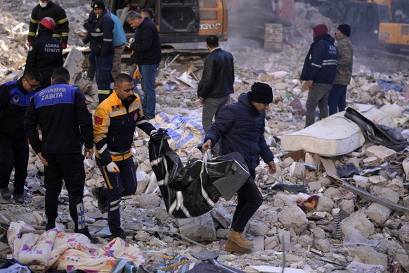 07.02.2023, Türkei, Adana: Zwei Männer tragen eine Leiche aus einem zerstörten Gebäude. Mehr als 13 Millionen Menschen in der Türkei sind nach Einschätzung der Regierung von der Erdbebenkatastrophe be ...