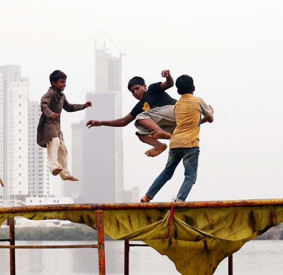 Children play on a trampoline, near electoral flag of a political party, with the under-construction buildings in the background, in a low-income neighborhood in Karachi, Pakistan July 18, 2018. REUTE ...