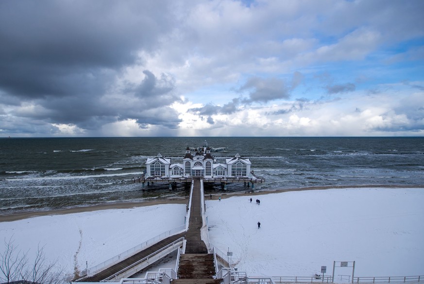 11.02.2021, Mecklenburg-Vorpommern, Sellin: Spazierg�nger sind am Strand vor der Seebr�cke unterwegs. Frostwetter und Schneefall behindern den Verkehr in Norddeutschland. Foto: Jens B�ttner/dpa-Zentra ...