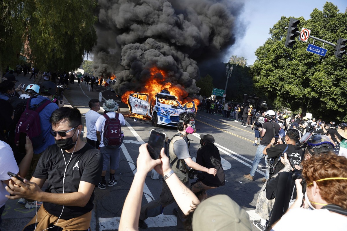 People watch while several Waymo cars burn in downtown Los Angeles after being vandalized by protesters reacting to a series of immigration raids that occurred in Los Angeles, Calif., on Sunday, June  ...