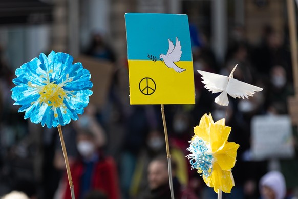 In Frankfurt werden Schilder mit Friedenstaube und Blumen in den Farben der Ukraine hochgehalten.