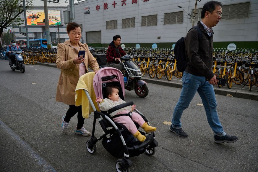 BEIJING, CHINA - APRIL 13: A woman looks at her mobile phone as she pushes a child in a stroller on a street April 13, 2023 in Beijing, China. (Photo by Kevin Frayer/Getty Images)
