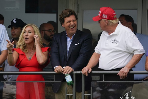 U.S. Rep. Marjorie Taylor Greene, left, Tucker Carlson, center, and former President Donald Trump, right, react during the final round of the Bedminster Invitational LIV Golf tournament in Bedminster, ...