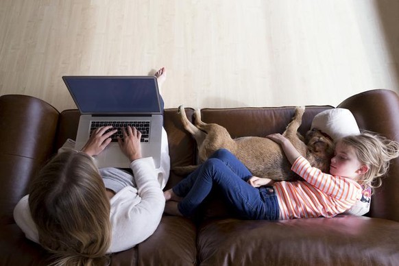 Ariel view of a woman using a laptop whilst her daughter is sleeping next to her, cuddling their pet dog.