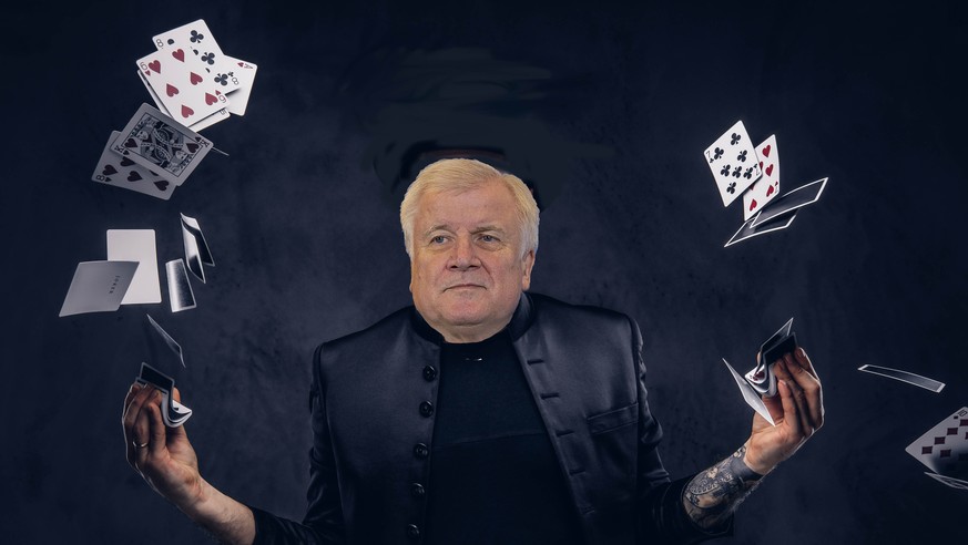 Magician in a black suit, sunglasses and top hat, showing trick with playing cards on a dark background.