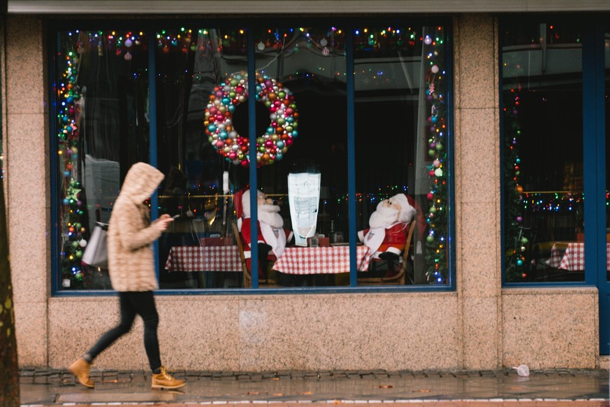 two Santa Claus dolls are seen inside a closing restaurant as a woman walks, in Cologne, Germany, on December 15, 2020. (Photo by Ying Tang/NurPhoto)