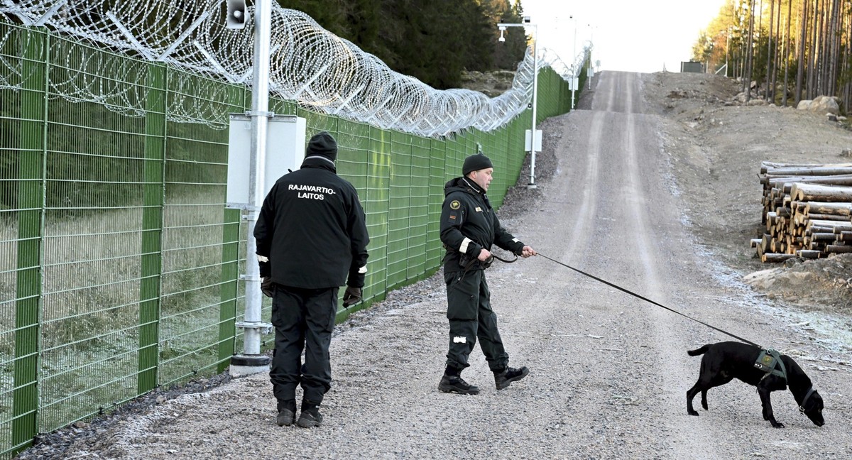 26.10.2023, Finnland, Imatra: Grenzschutzbeamte und ein Hund stehen am Grenzzaun während einer Medienveranstaltung des finnischen Grenzschutzes RAJA an der finnisch-russischen Grenze. In Finnland schr ...