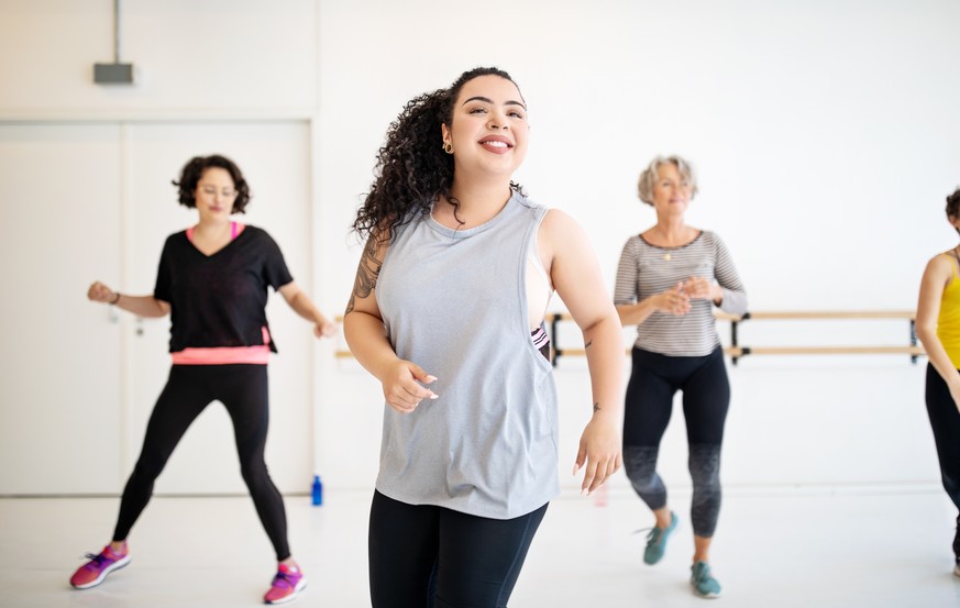 Young woman learning dance moves in fitness class. Multi-ethnic women dancing in studio.