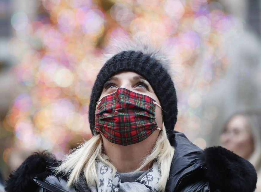 A woman wears a tartan fabric face mask while looking at the Saks Fifth Avenue Christmas decorations near the Rockefeller Center Christmas Tree in New York City on Tuesday, December 21, 2021. New York ...