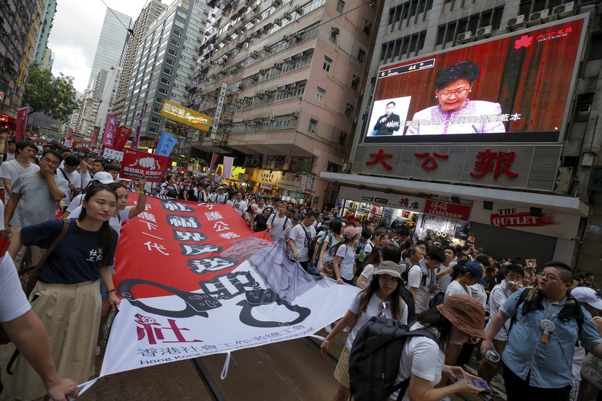 Protesters hold banner march past a TV screen broadcasting Hong Kong Chief Executive Carrie Lam delivering a speech during a rally against the proposed amendments to an extradition law in Hong Kong Su ...
