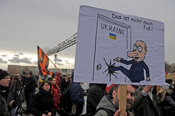 Dec. 13, 2014 - Berlin, Berlin, Germany - A demonstrator hold a caricature of Putin at rally called Friedenswinter at 13.12.2014 in Berlin, Germany in the air while the Sankt-Georgs-Flag is flying in  ...