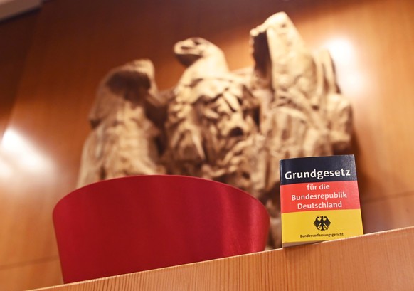 ILLUSTRATION - Vor dem Bundesadler im Sitzungssaal des Bundesverfassungsgericht steht eine Miniaturausgabe des Grundgesetz für die Bundesrepublik Deutschland sowie ein Barett eines Bundesverfassungsri ...