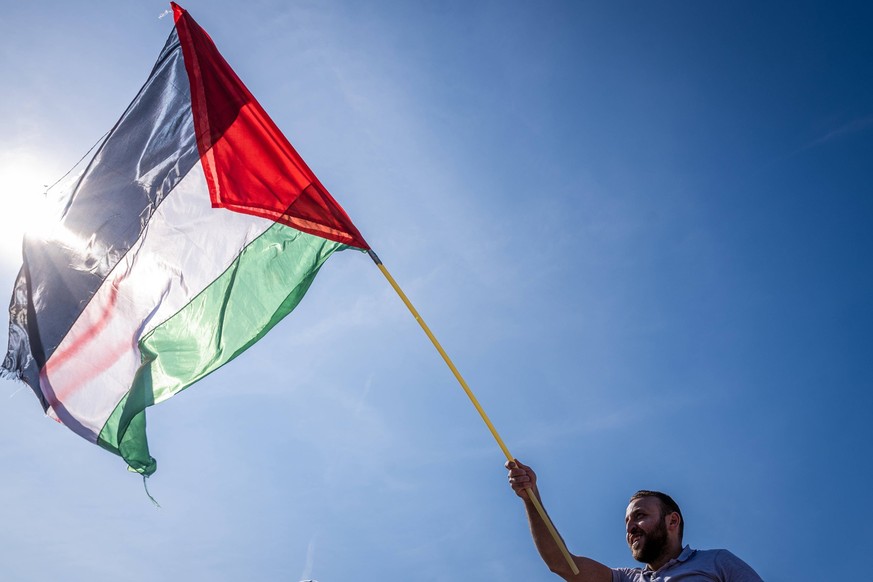 May 11, 2024, Amsterdam, North Holland, Netherlands: A demonstrator waves the flag of Palestine as the sun shines bright in the background. On May 11, 2024, several thousand pro-Palestinian demonstrat ...