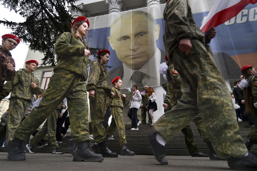 17.03.2023, ---, Jalta: Uniformierte Jugendliche marschieren anlässlich einer Aktion zum neunten Jahrestag der Krim-Annexion an einem Bildnis des russischen Präsidenten Wladimir Putin (im Hintergrund) ...