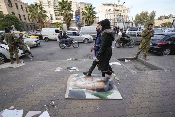 10.12.2024, Syrien, Damaskus: Fußgänger gehen über ein Bild des ehemaligen syrischen Präsidenten Assad das auf einem Bürgersteig liegt. Foto: Hussein Malla/AP/dpa +++ dpa-Bildfunk +++