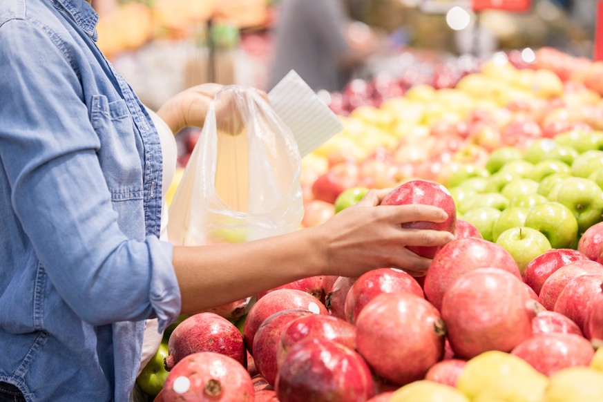 Unrecognizable woman picks out a pomegranate while shopping in a grocery store.