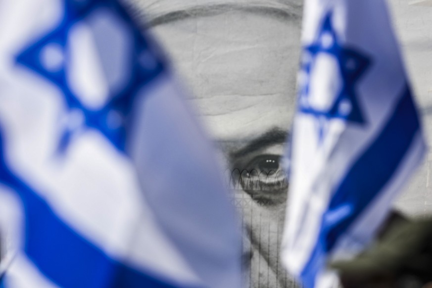 22.02.2023, Israel, Jerusalem: Ein Transparent mit einem Bild des israelischen Premierministers Netanjahu ist hinter Fahnen zu sehen, die von Demonstranten während eines Protestes gegen die Justizrefo ...